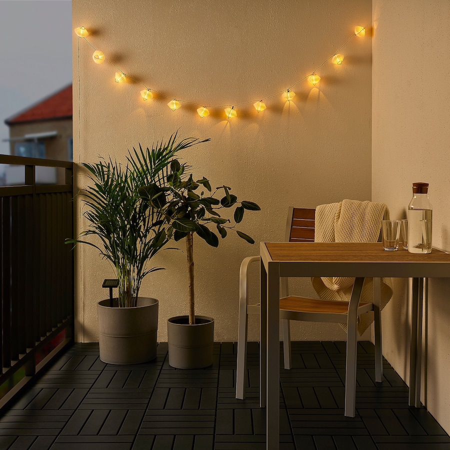 Lichterkette auf einem Balkon mit zwei Topfpflanzen, kleinem Tisch und Stuhl