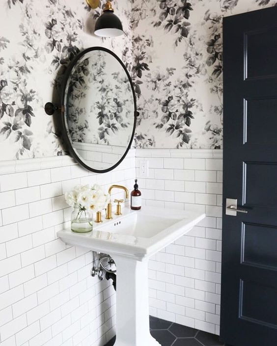 Lavabo de pedestal bajo un espejo circular en el baño con papel pintado floral