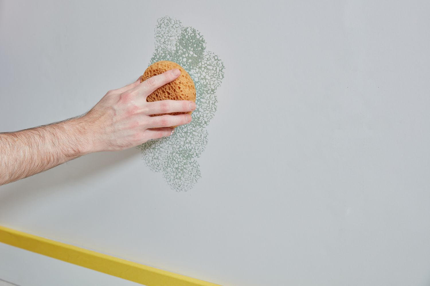 Esponja pressionando levemente a tinta verde nas paredes