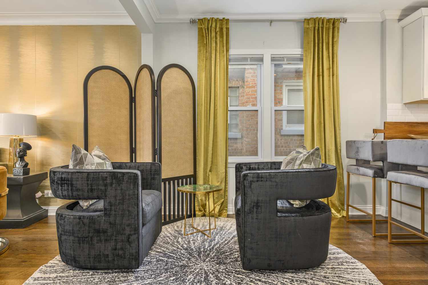 Eine Sitzecke mit einem Rattan-Raumteiler, einem gelben Vorhang, der bis zur Decke reicht, und schwarzen Stühlen