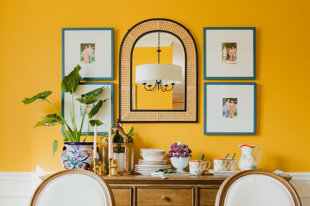 Gelbes Esszimmer mit blauen Bilderrahmen und Stockspiegel