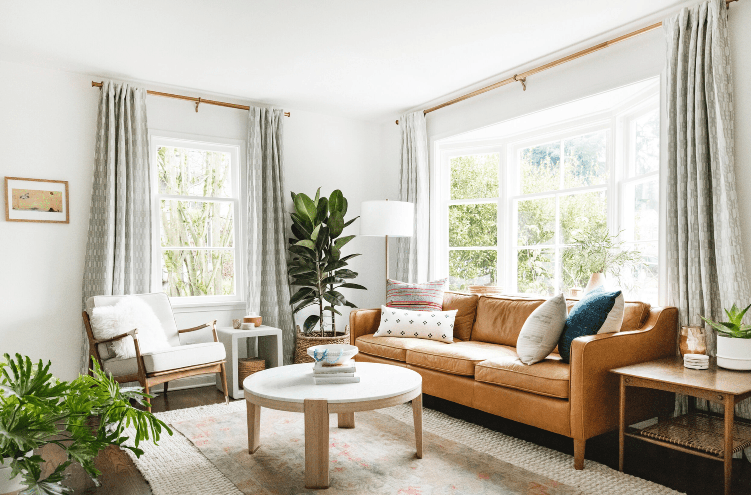 Ein Wohnzimmer mit einem Couchtisch, einem Sessel und einem Ledersofa, das so breit ist wie das riesige Erkerfenster des Raumes