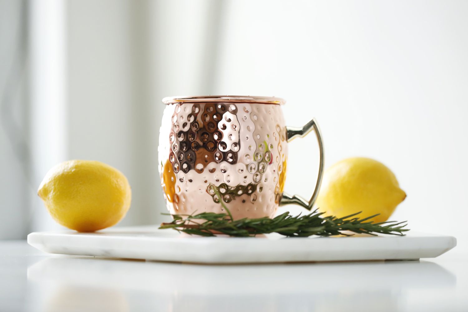 Tasse en cuivre avec deux citrons et un brin de romarin sur une assiette blanche