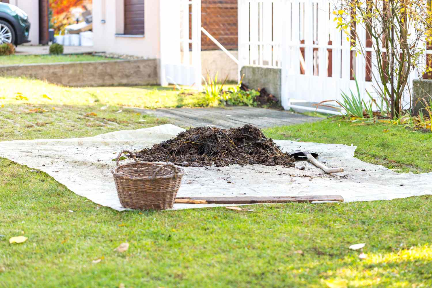 Kleiner Haufen verfaulter Gülle auf einer Plane im Vorgarten. Gartenschaufel und Korb in der Nähe des Haufens. Organischer Dünger zum Düngen des Bodens, bereit für die Arbeit im Herbstgarten. Konzept des ökologischen Landbaus