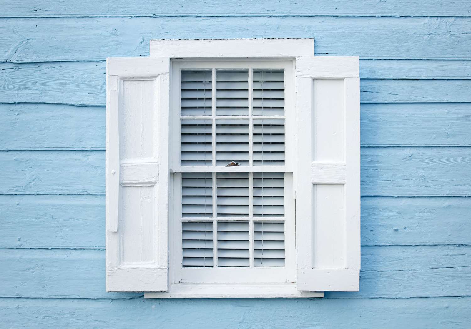 persianas brancas de painel plano em janela branca e casa azul