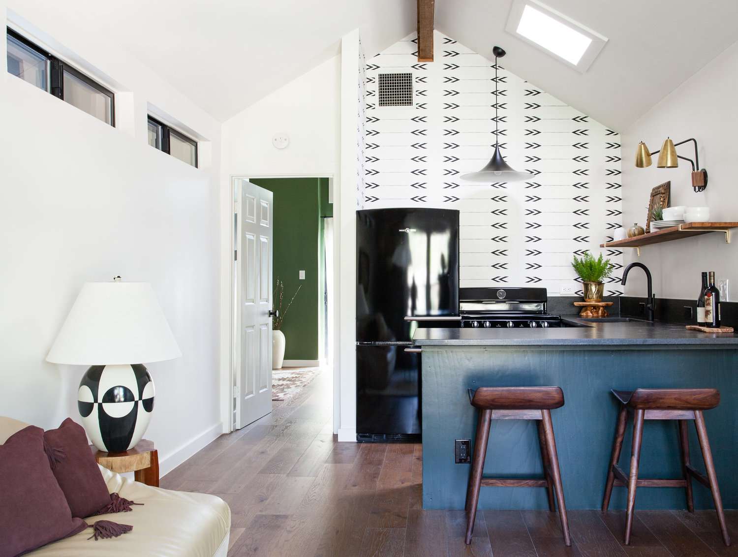 Cozinha com papel de parede gráfico e armários inferiores pintados de azul abertos para a sala de estar