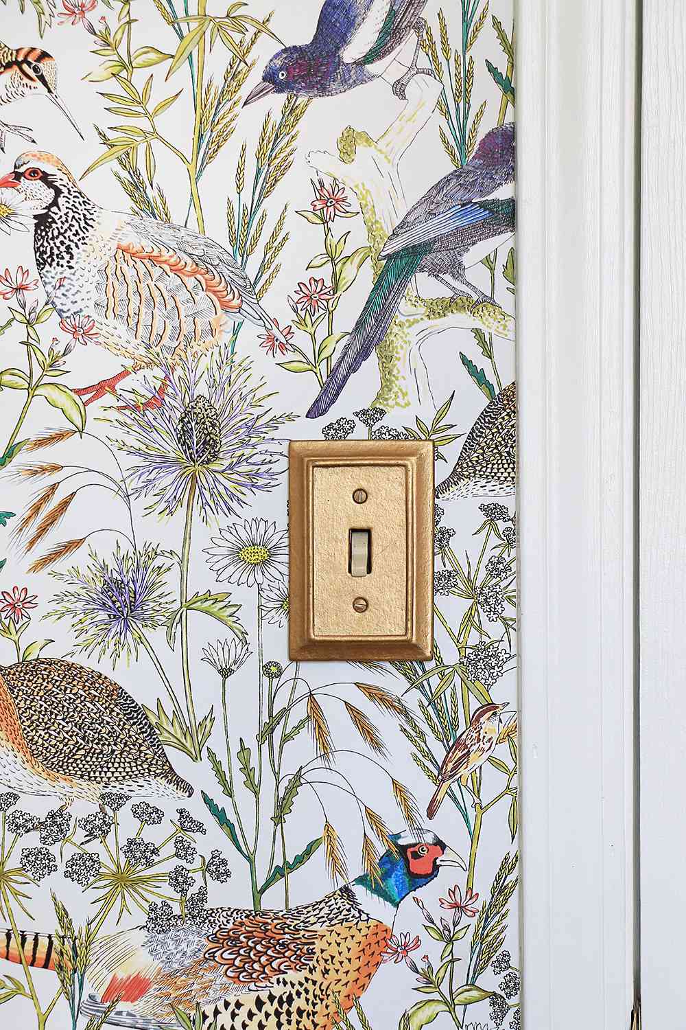 Primer plano de papel pintado con pájaros y flores y un interruptor de luz dorado