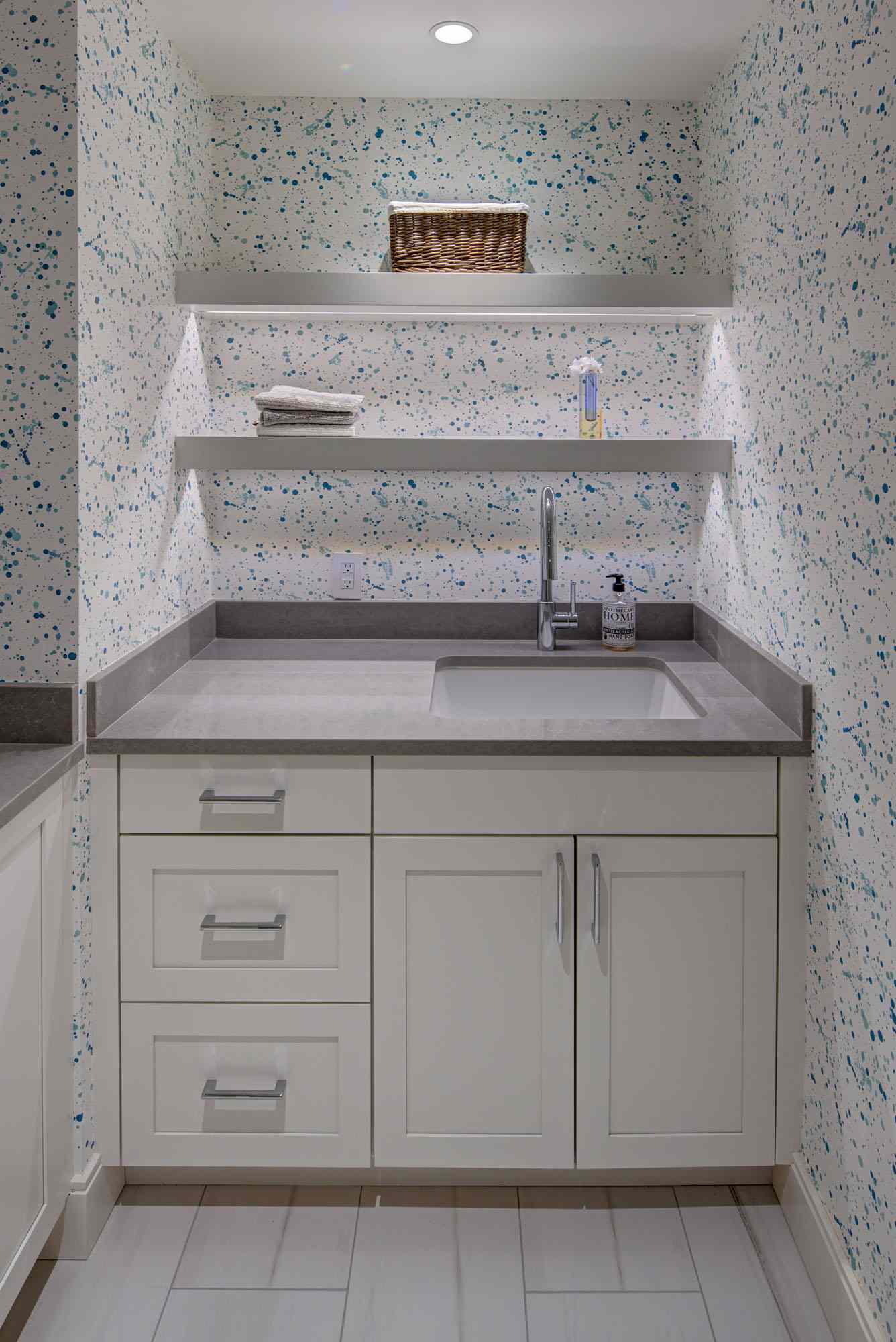 Paint splatter style wallpaper in a laundry room with white cabinets and floating shelves