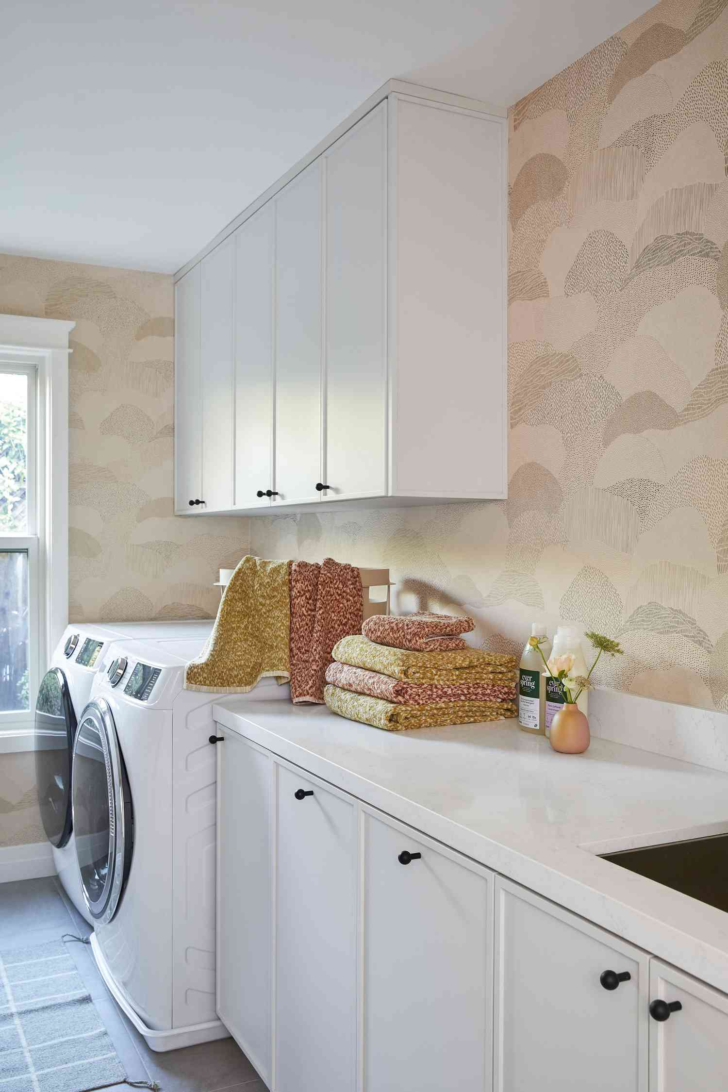 Lavanderia com papel de parede cor de pêssego e armários brancos