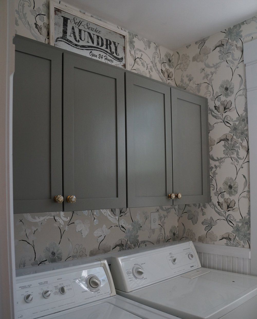 Papel de parede com estampa floral em uma lavanderia com armários cinza