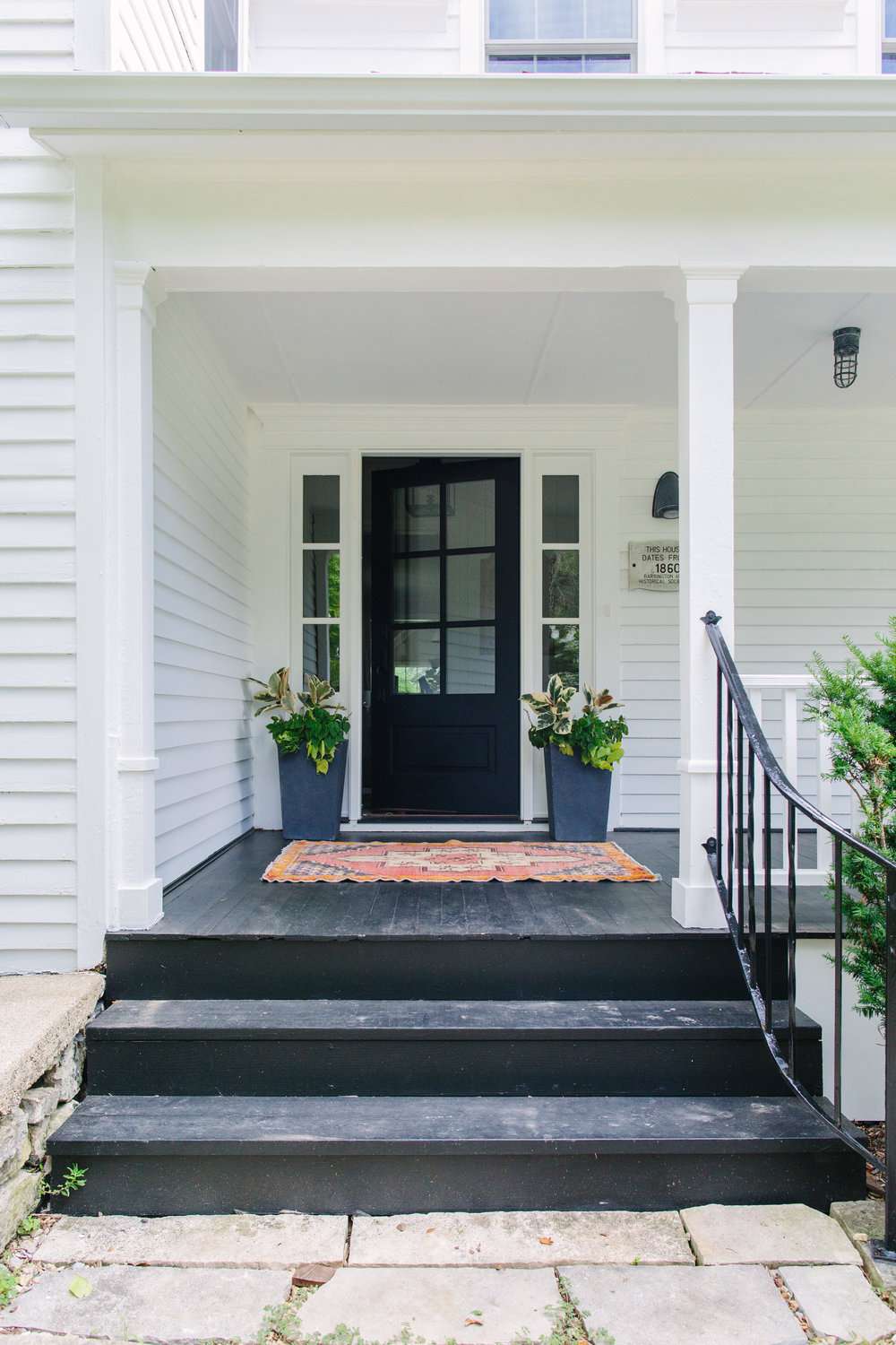 Weißes Haus mit schwarzer Tür und schwarz gestrichener Veranda und Treppe