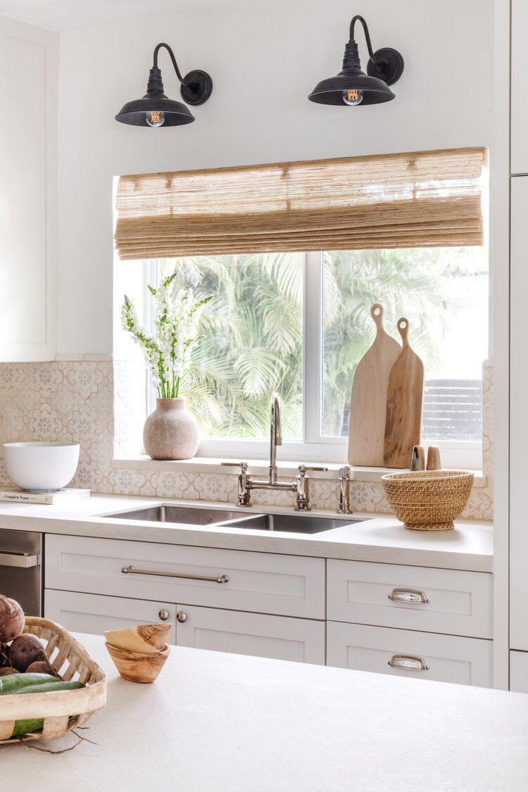 Una cocina color melocotón con una ventana decorada con persianas tejidas de color beige, una olla beige y dos tablas de cortar de madera clara
