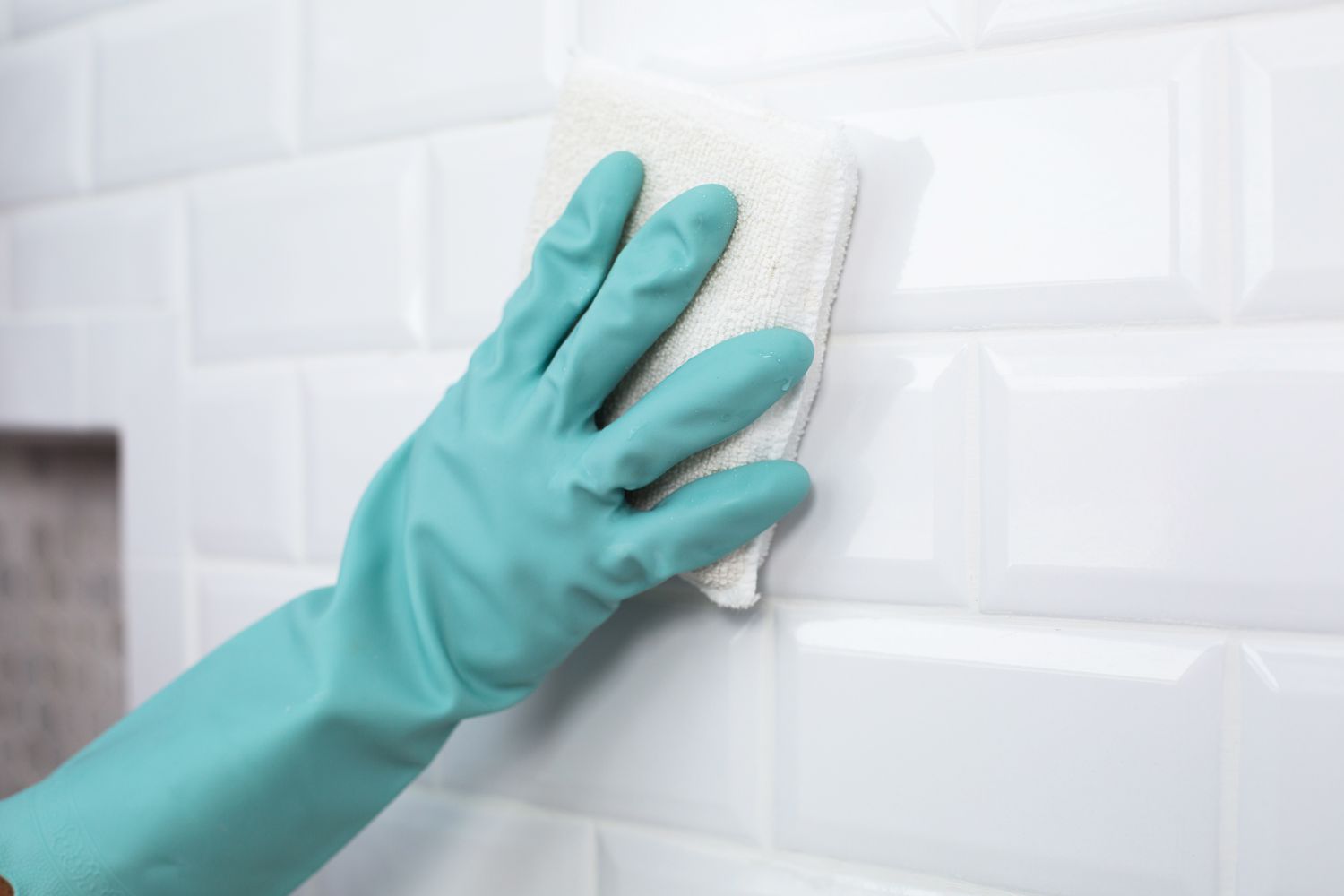 Fugenschleier von weiß gefliester Wand mit weißem Schwamm und blaugrünen Handschuhen gereinigt