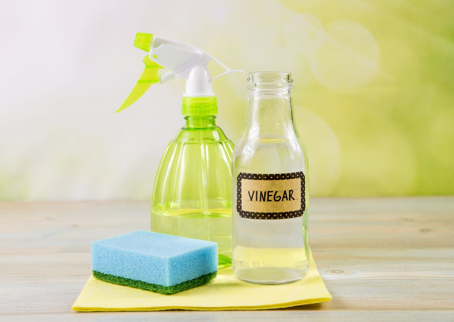 Concepto de productos de limpieza del hogar sin productos químicos. Uso de vinagre blanco destilado natural en botella de spray para eliminar manchas. Herramientas sobre mesa de madera, fondo verde bokeh, espacio de copia.