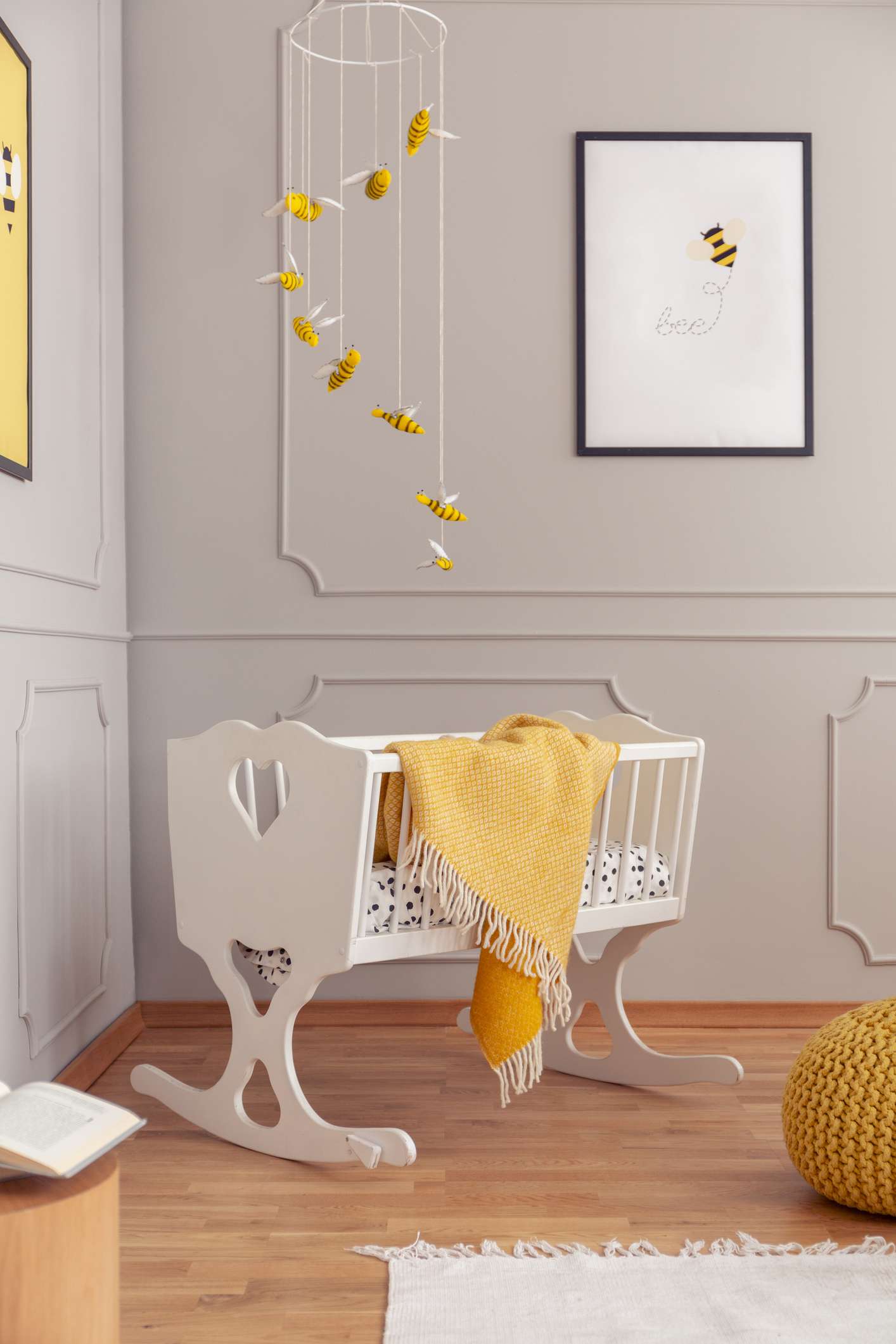 Abeilles au-dessus d'un berceau en bois blanc dans une chambre de bébé grise avec poster sur le mur vide