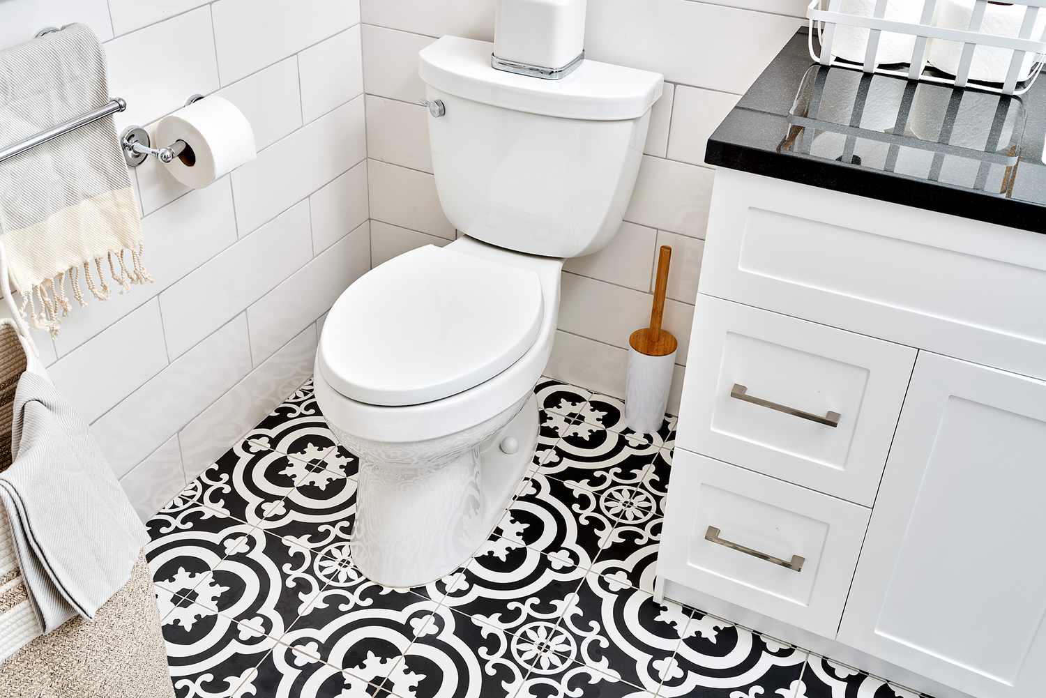 Inodoro estándar con descarga por gravedad rodeado de suelo de baldosas con motivos blancos y negros en el baño