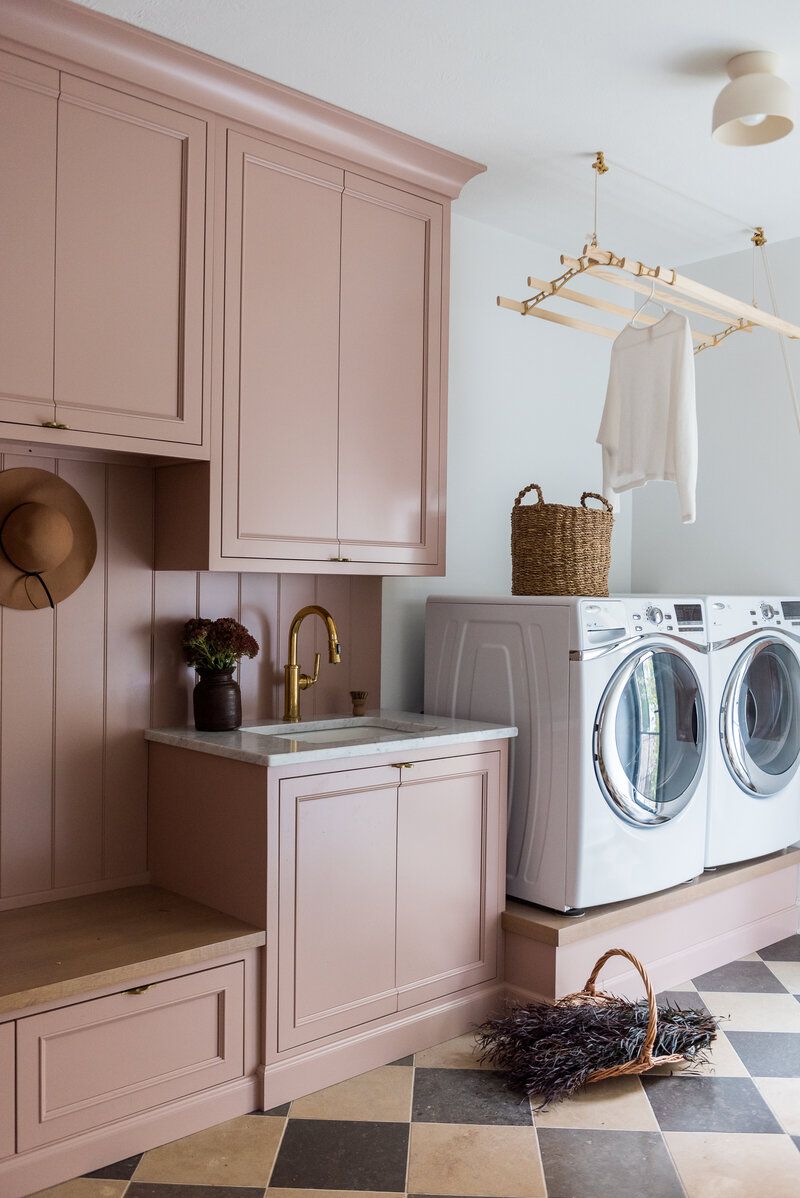 Waschmaschine und Trockner auf einer Steigleitung in einer Waschküche mit rosa Schränken