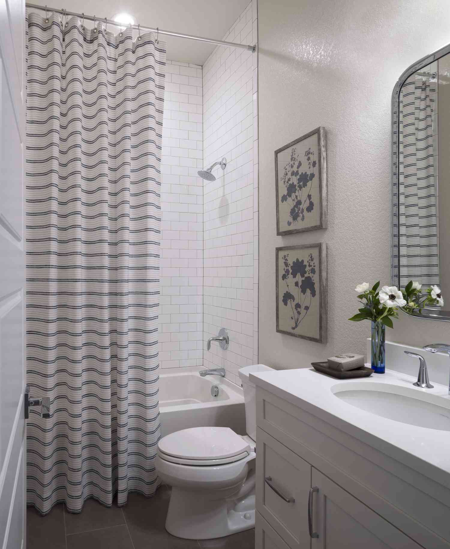 Ein weißes Badezimmer hat einen gestreiften Duschvorhang und zwei beige Bilder mit blauen Blumen, die zum gestreiften Vorhang passen