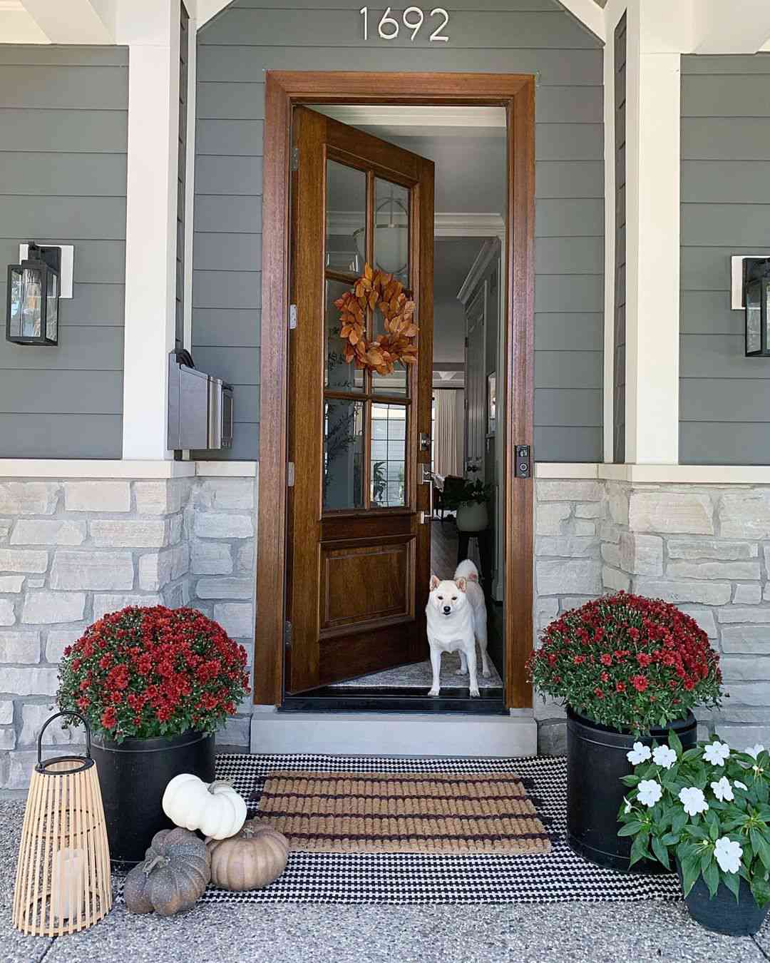 Veranda im Landhausstil mit hölzerner Eingangstür, geschichteten Matten und Herbstdekor
