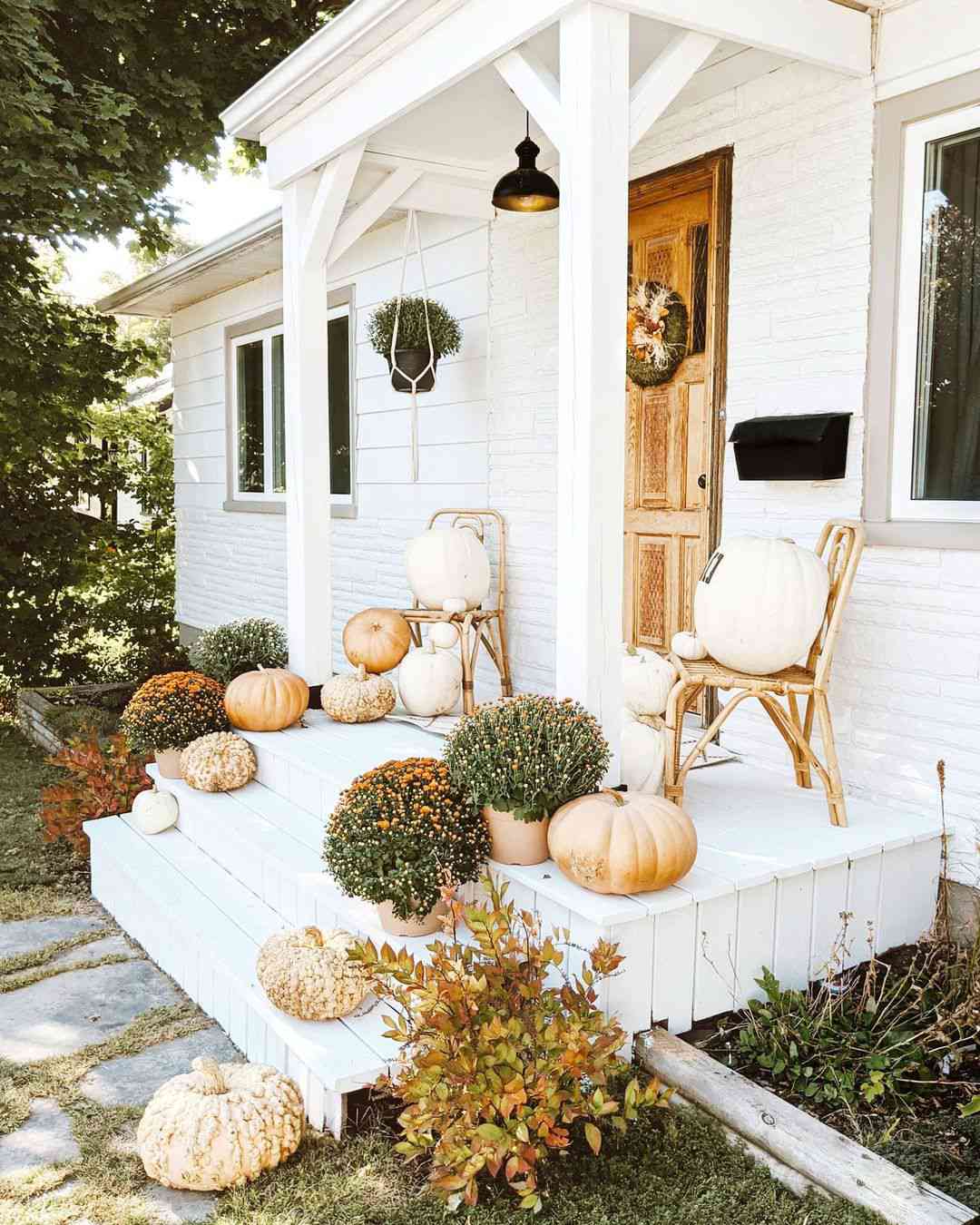 Porche peint en blanc avec des chaises en rotin et décor d'automne sur les marches
