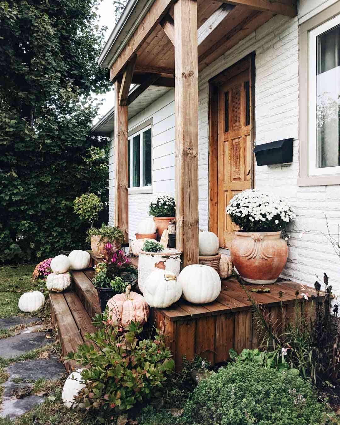 Granja blanca con porche de madera y decoración otoñal en los escalones de entrada