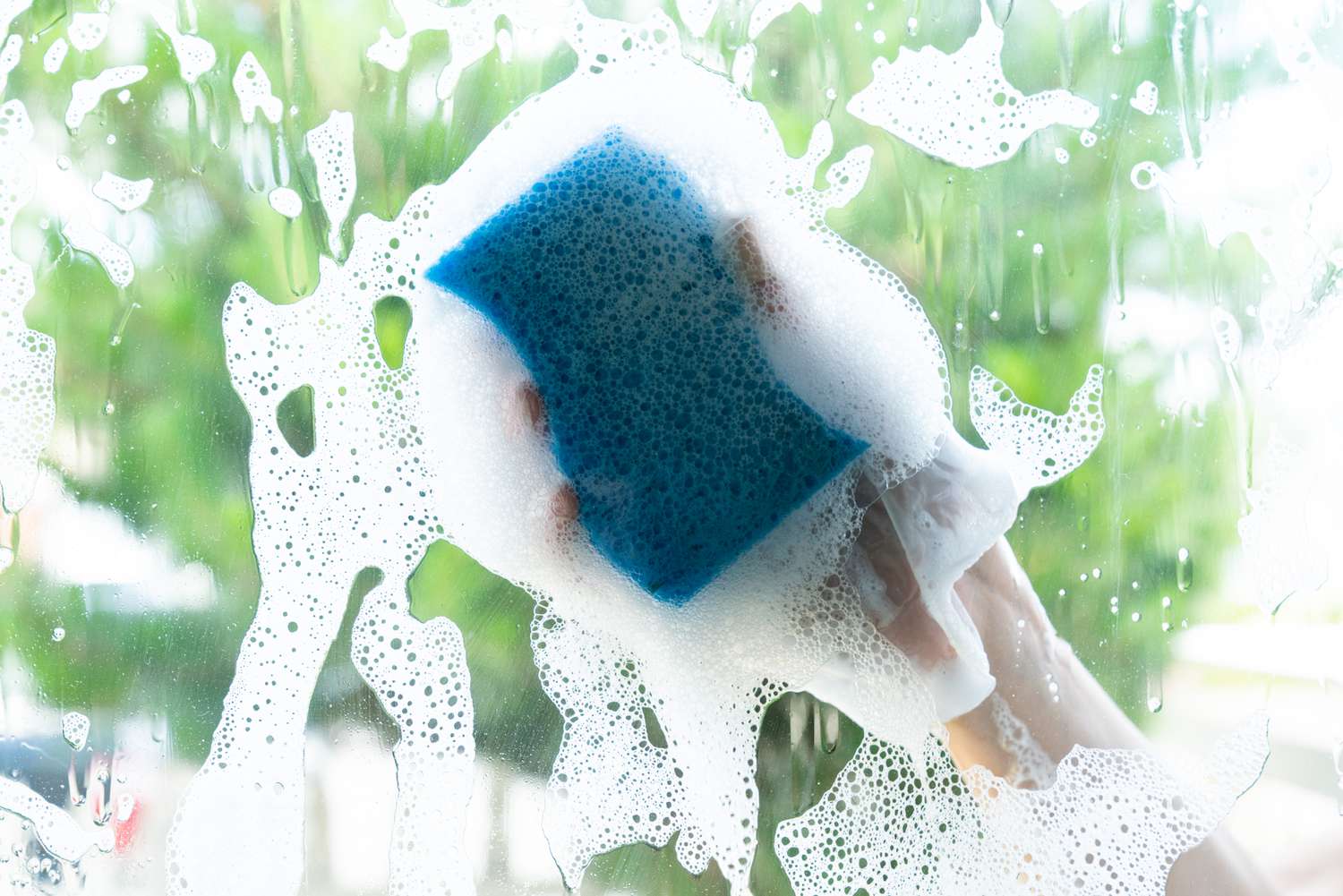 Janela limpa do lado de fora com esponja azul e água com sabão