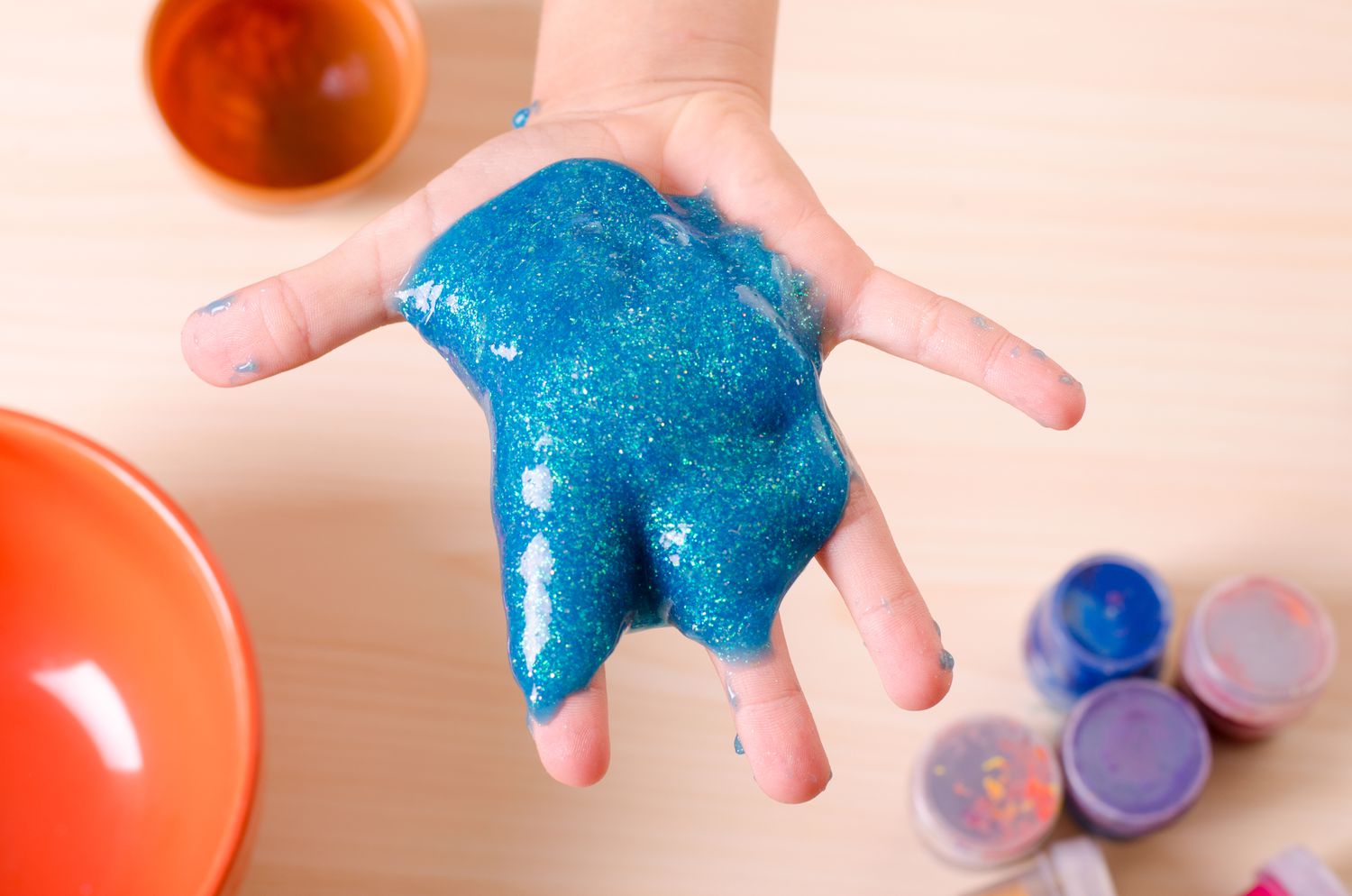 Kinderhand hält glitzernden blauen Schleim