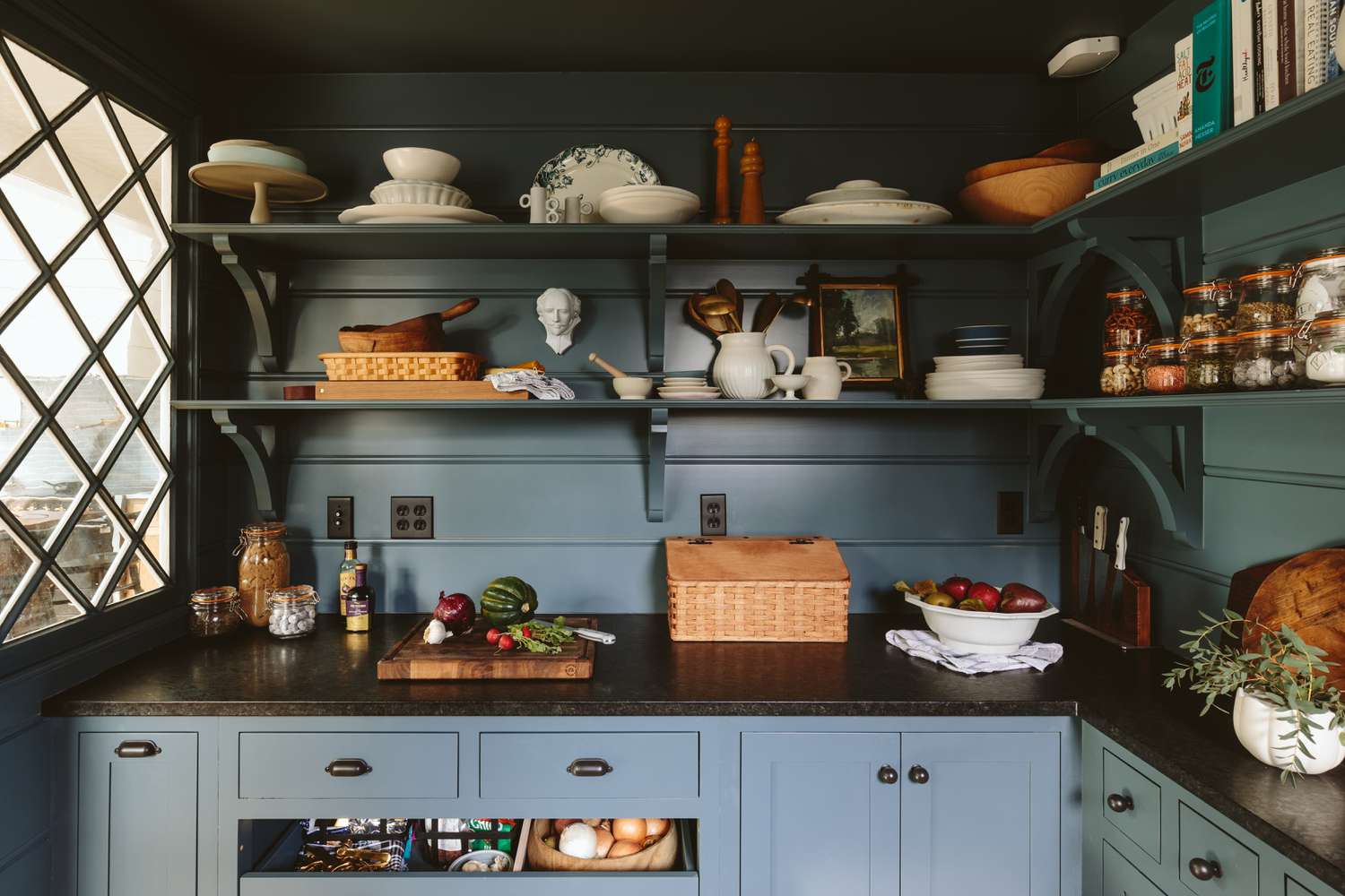 Blue cabinets covered in dark countertops fit this pantry