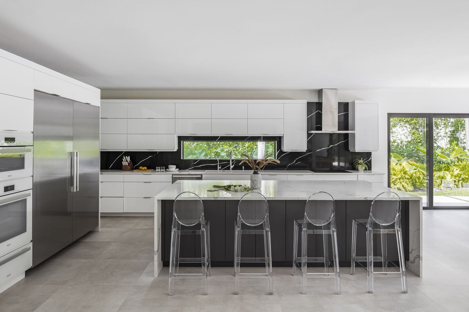 Grauer Bodenbelag bedeckt eine Küche, die auch schlichte weiße moderne Schränke ohne Knöpfe umfasst