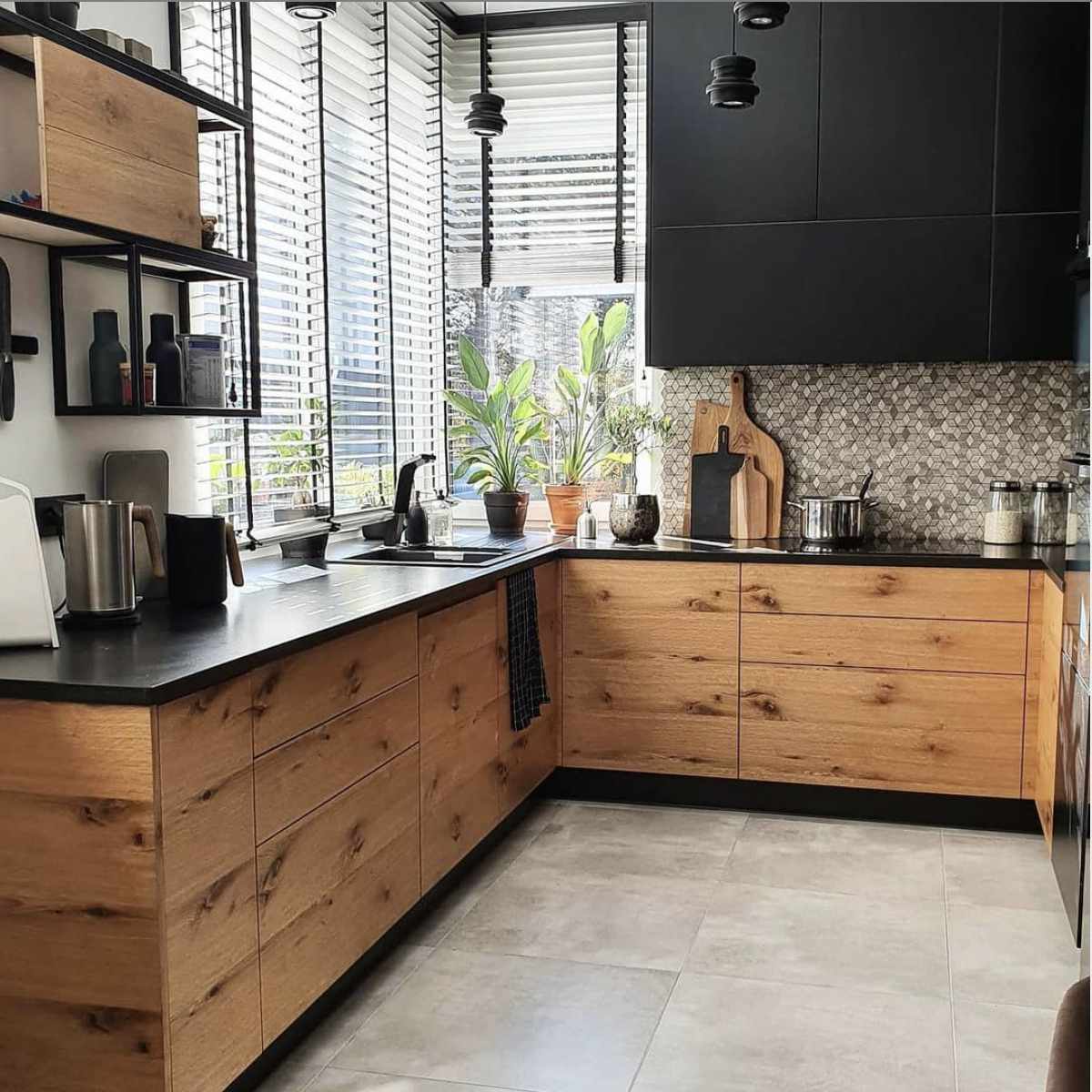 cocina con armarios inferiores de madera y superiores negros, suelo de baldosas grandes gris claro, accesorios negros, backsplash de baldosas romboidales grises y blancas