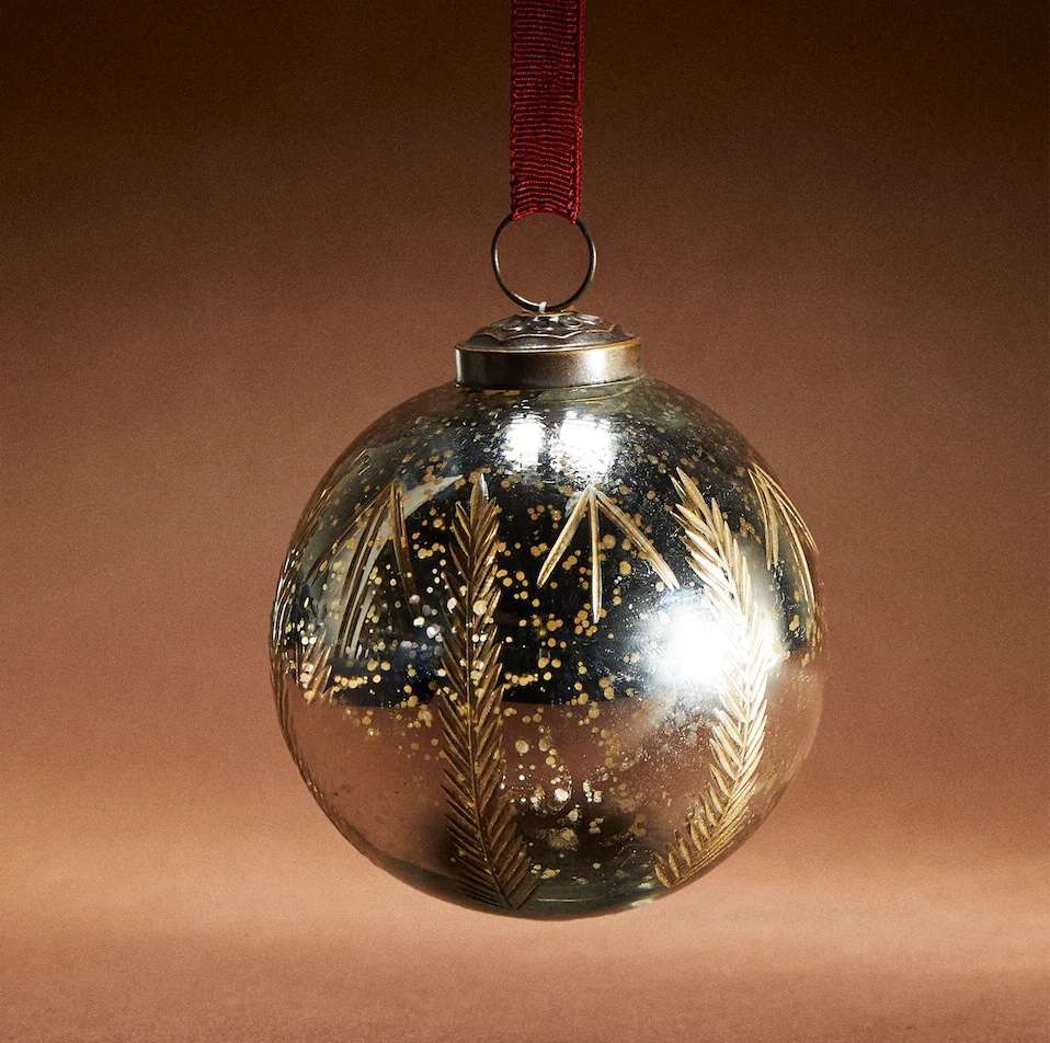Ornamento de bola de vidro simples com detalhes dourados em uma fita de veludo vermelho.