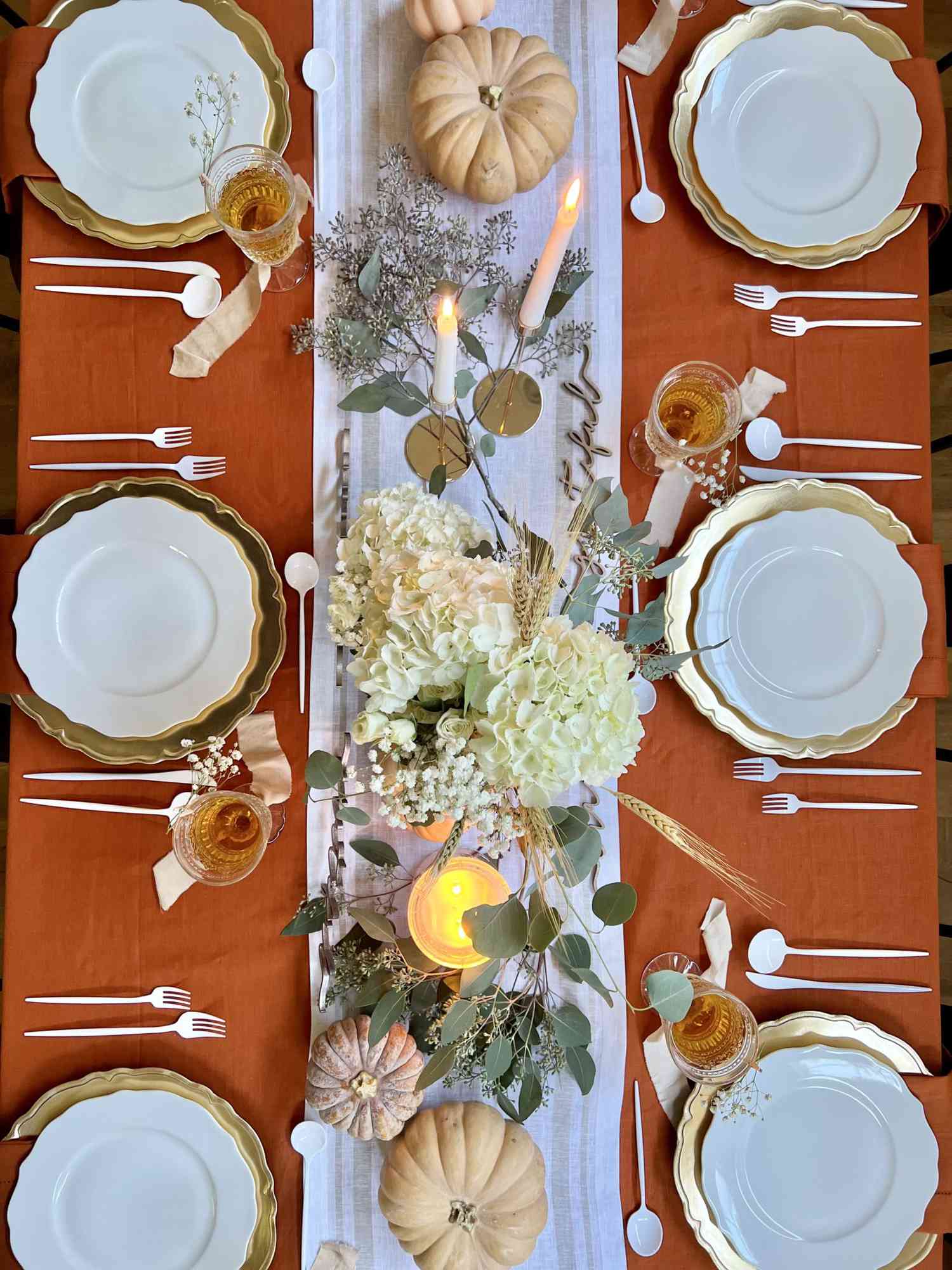 Overhead of a Thanksgiving-themed dinner table with decorative centerpieces and place settings