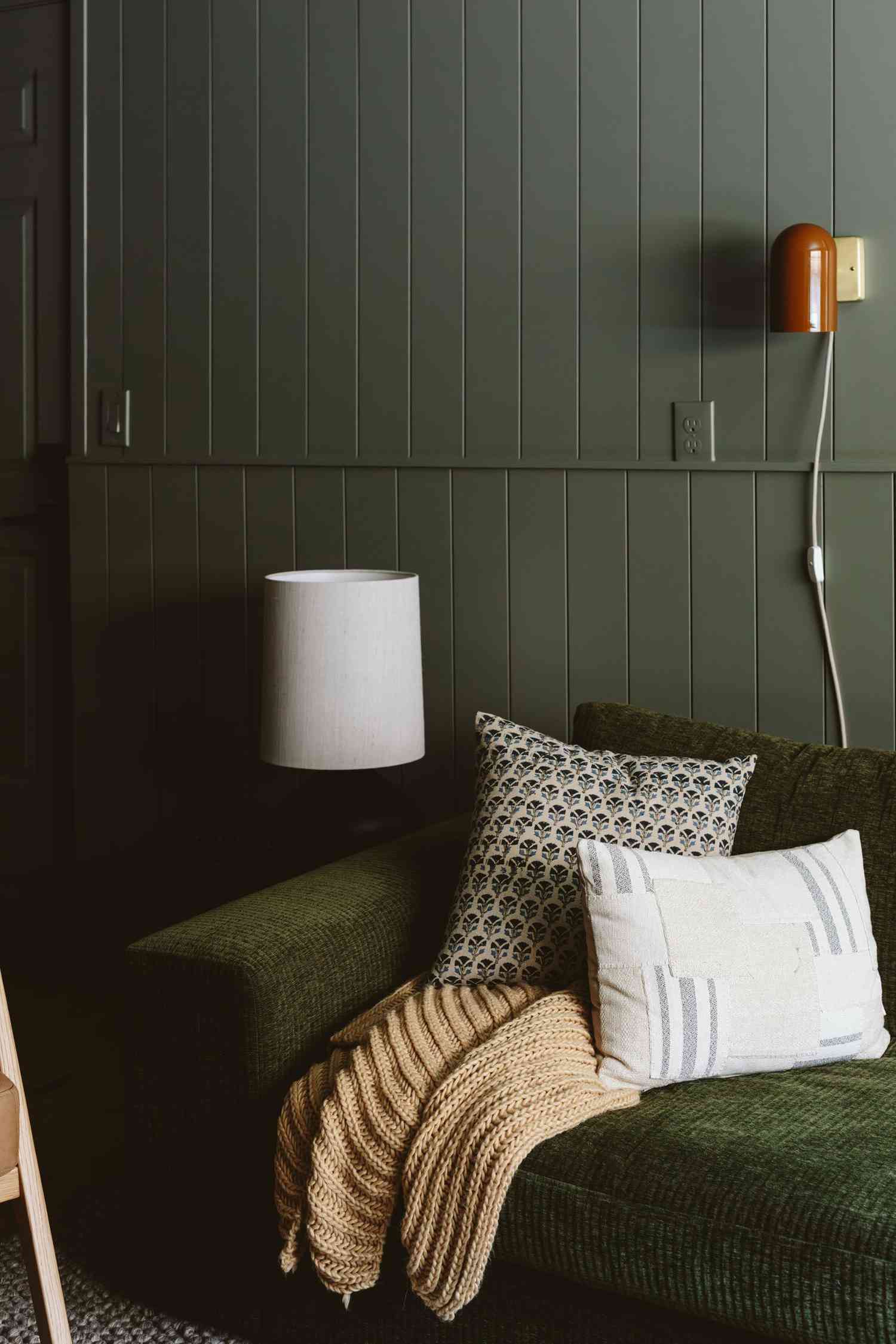 Dunkelgrüne Wand hinter einem Sofa mit Kissen und Überwurf