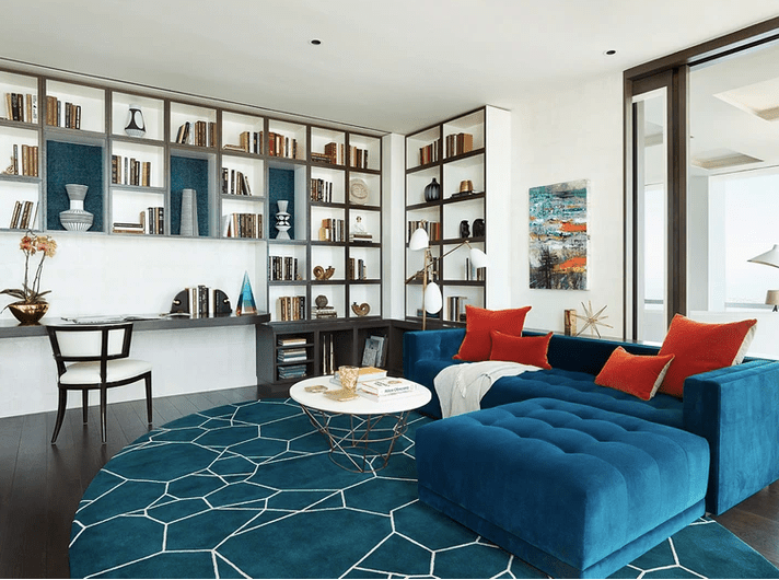Wohnzimmer mit tealfarbenem Rundteppich und Sektionssessel aus Samt mit cayennefarbenen Kissen