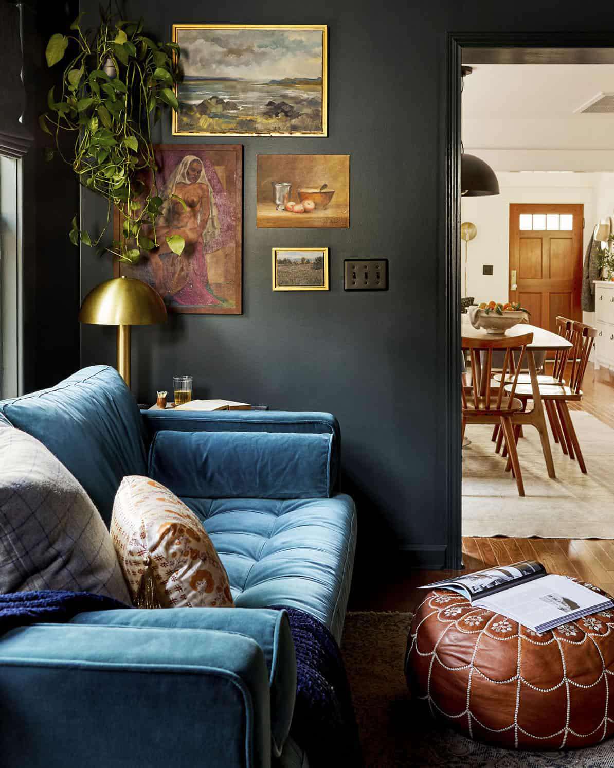 Sala de TV verde-escura com parede de galeria de pintura vintage e sofá de veludo azul-petróleo