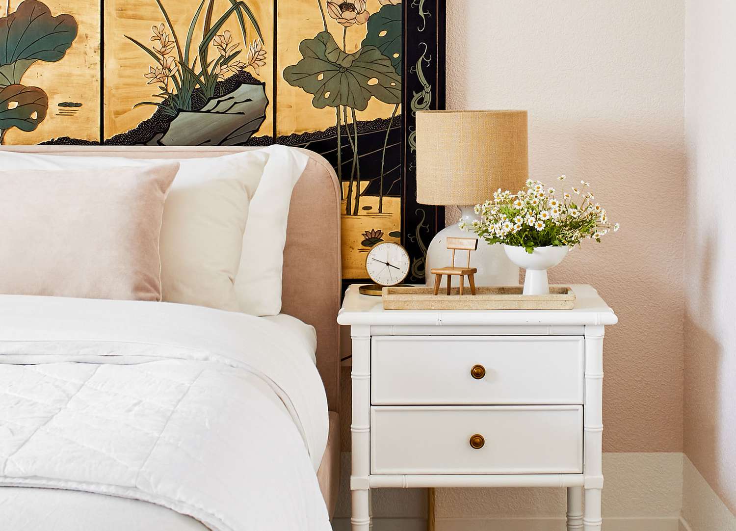A peach bedframe sits in front of a gold paneled wall artwork