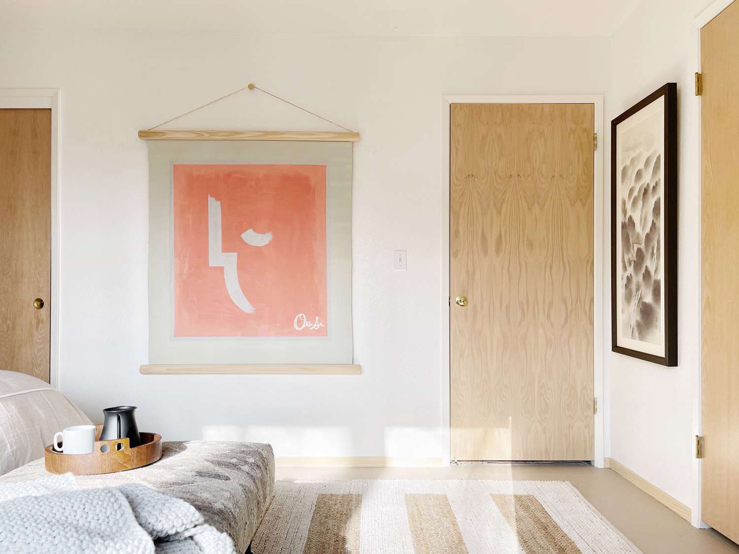 Helle Holztüren ergänzen einen pfirsichfarbenen Wandbehang, der ein helles, cremefarbenes Schlafzimmer bedeckt