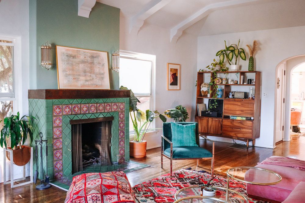 Sala de estar com lareira azul-petróleo e tapete marroquino rosa e vermelho, móvel de parede moderno de meados do século e mesa de centro pós-moderna de latão e vidro