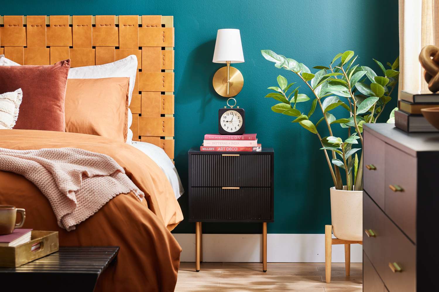 Teal bedroom with lattice leather headboard, black and brass nightstand, and a potted rubber plant