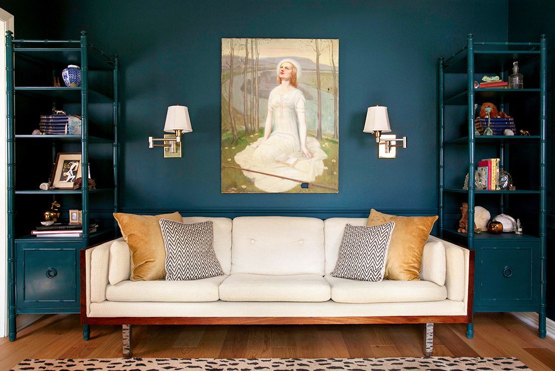 Sala de estar com paredes em azul-petróleo escuro, estantes de bambu falso, sofá branco e tapete de leopardo