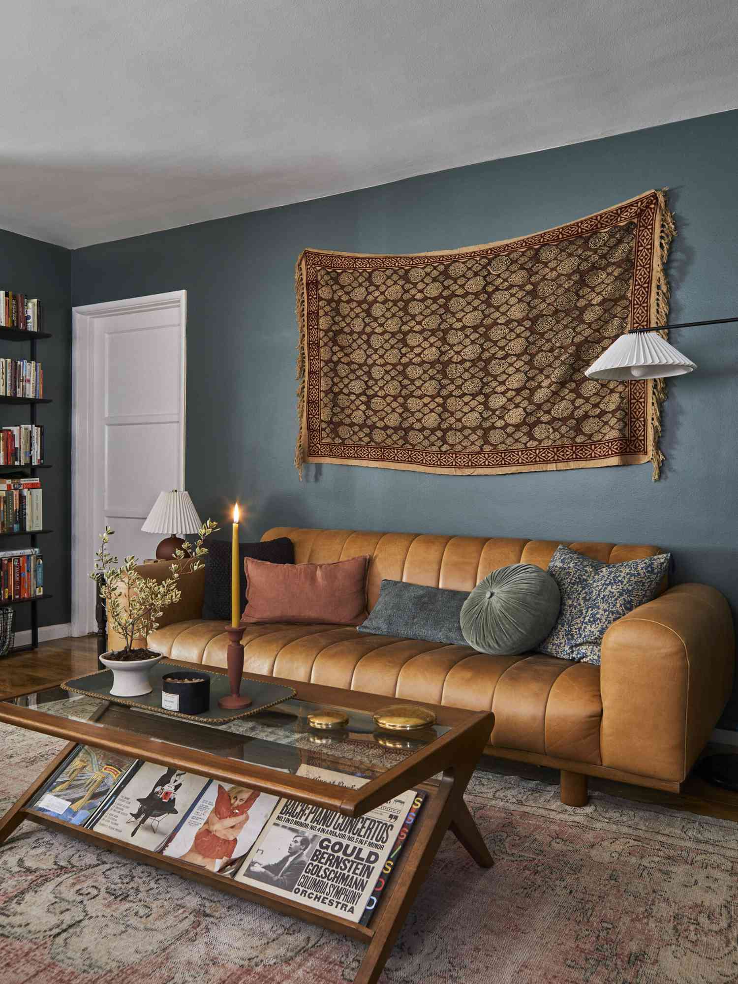 Salon sarcelle avec une tapisserie bordeaux accrochée au mur, canapé en cuir cannelé, et table basse de style italien Mid-Century Modern