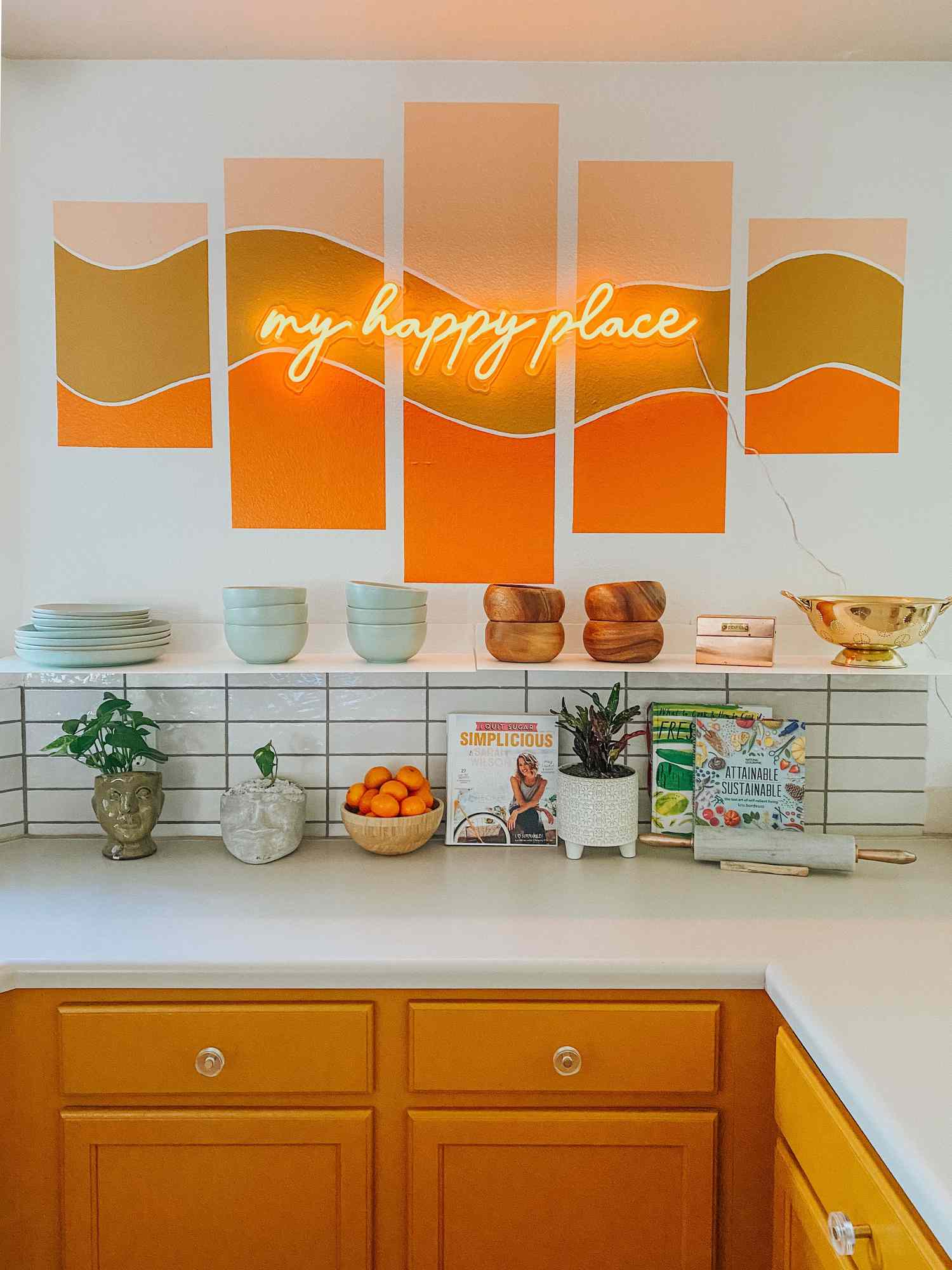 Tangerine orange colored kitchen cabinets are paired against a peach mural with a neon sign in peach