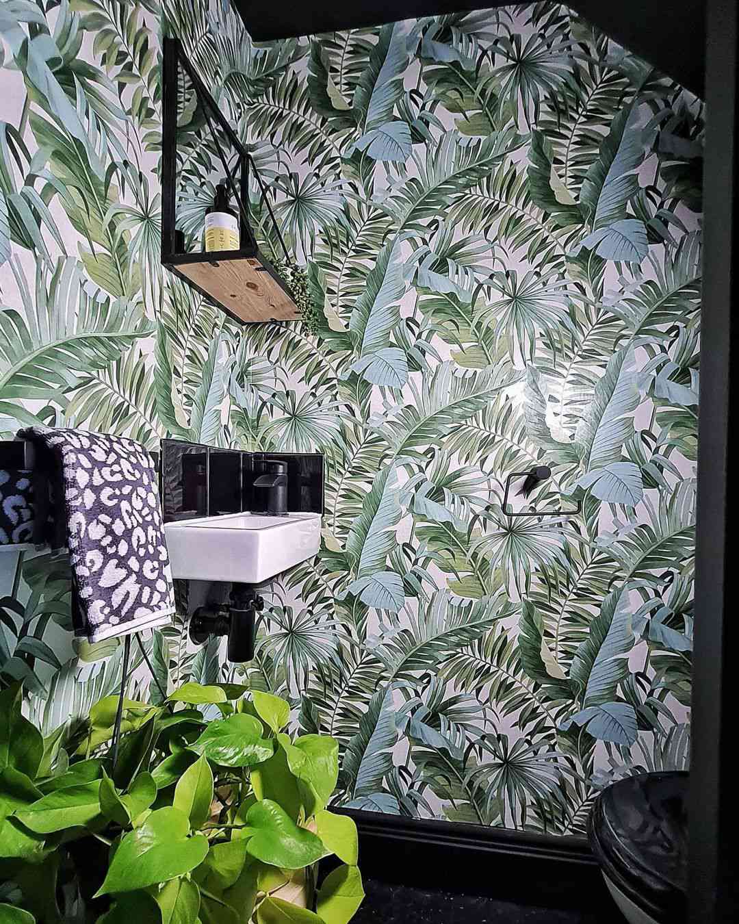 Baño pequeño con lavabo negro en esquina y papel pintado de palmeras