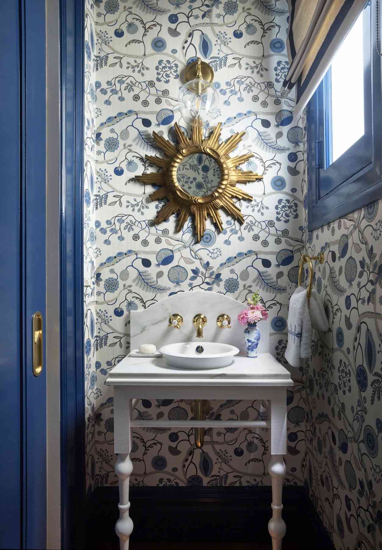 Salle de bain avec papier peint floral bleu, miroir en étoile, garniture bleue, petit lavabo avec robinet mural