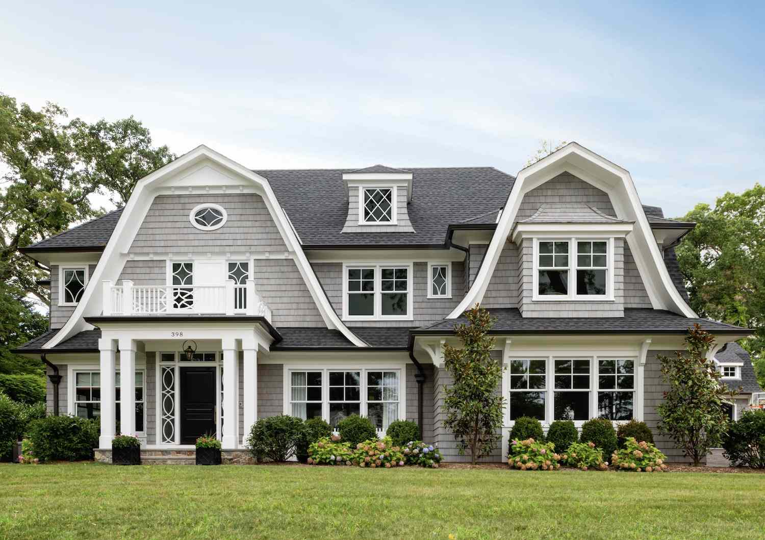 Grande maison coloniale Ducth avec entrée à piliers et plantations de divers arbustes devant