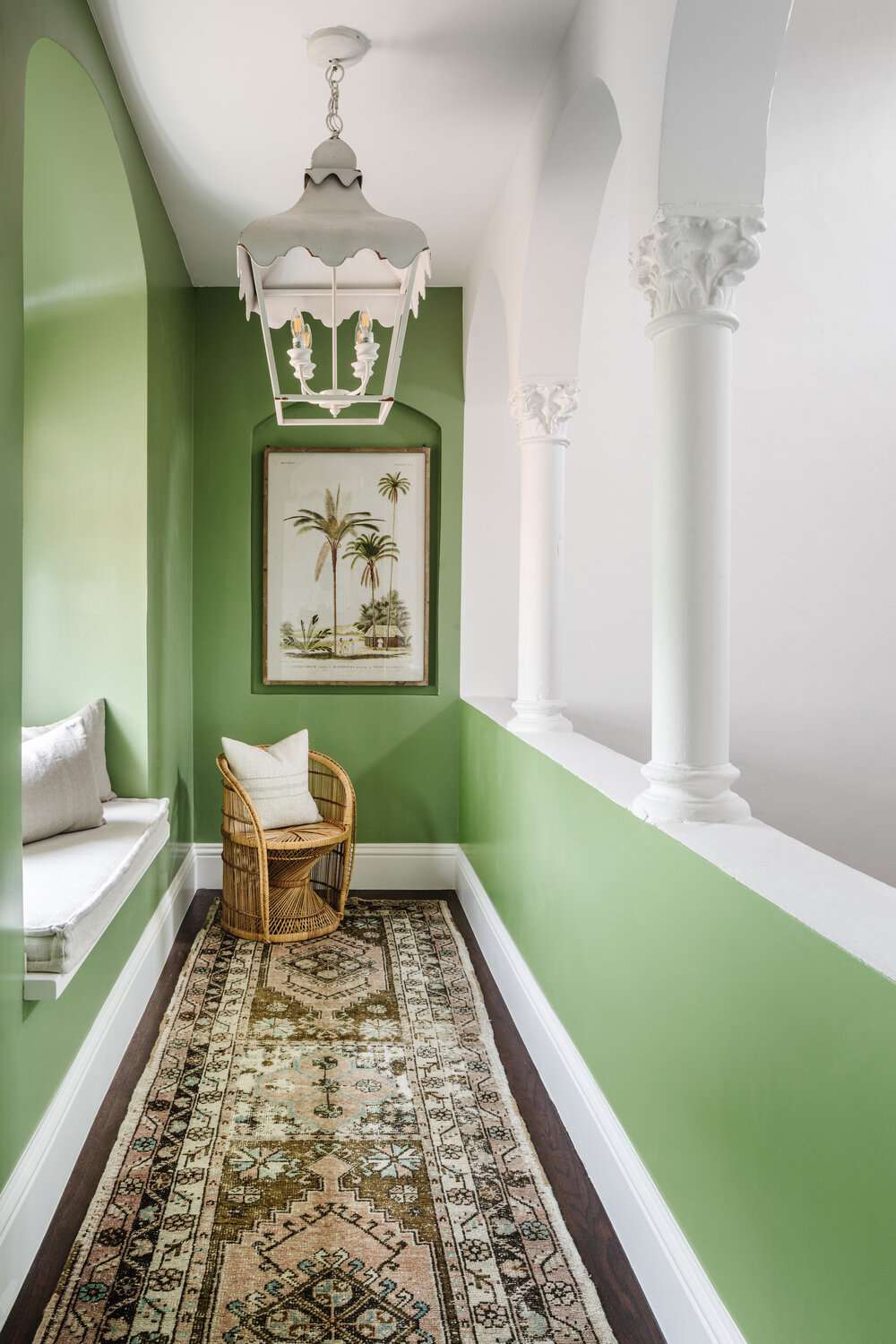 Corredor verde com um assento na janela e uma luminária pendente branca ornamentada