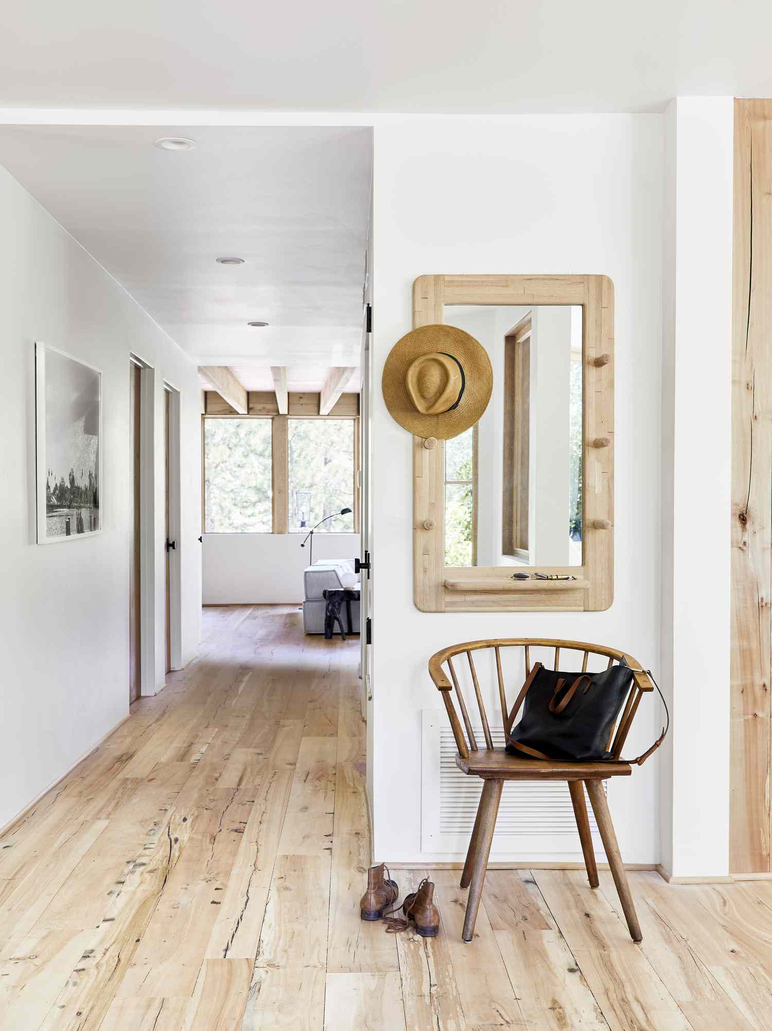 Corredor branco com piso de madeira e uma cadeira e espelho de madeira