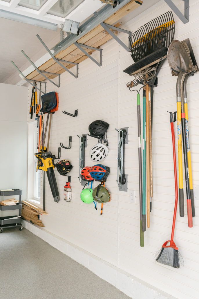 Capacetes e ferramentas de jardinagem pendurados em ganchos na parede de uma garagem