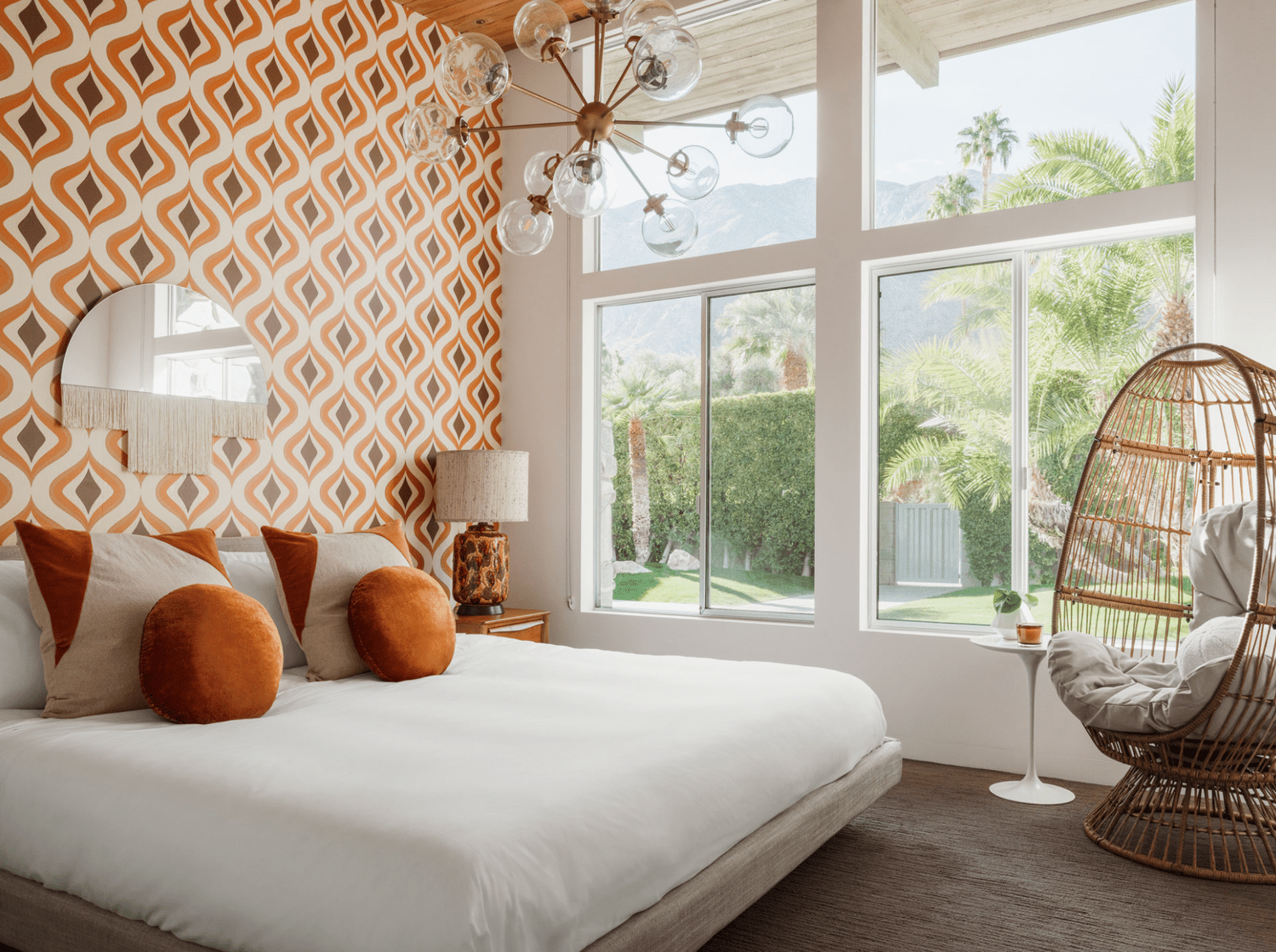 Ein modernes Art-Deco-Schlafzimmer mit orangefarbener Tapete, orangefarbenen Kissen und einem Starburst-Kronleuchter