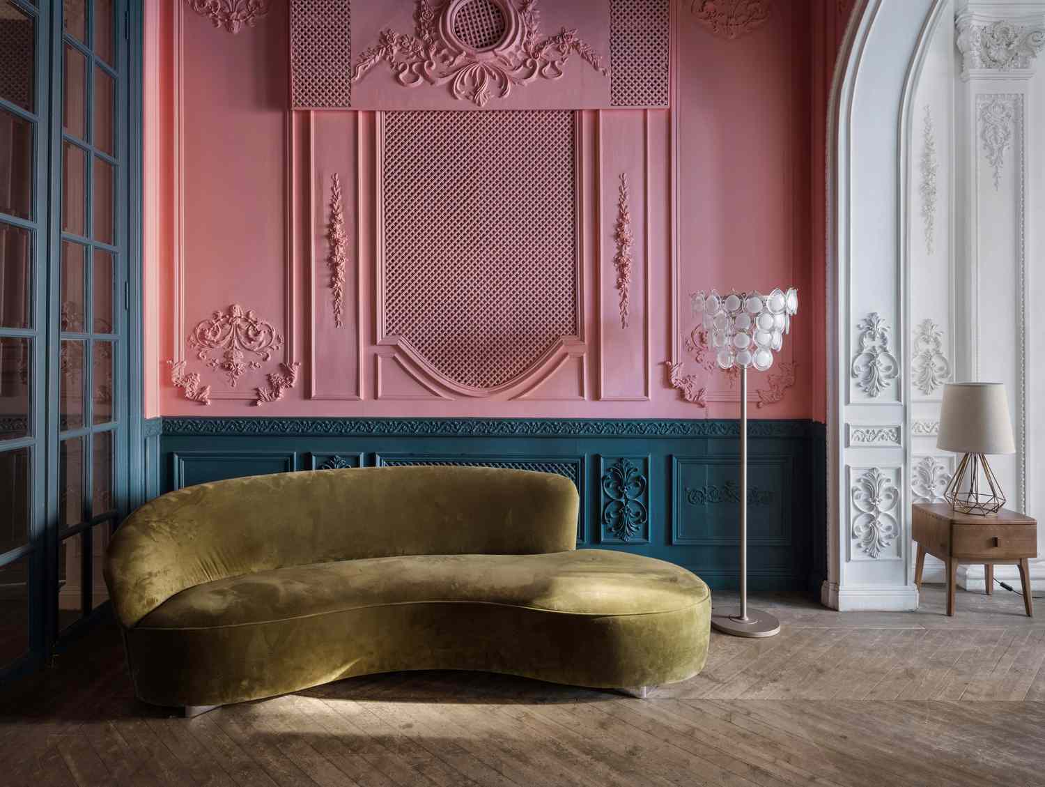 Ein geschwungenes Sofa aus grünem Samt mit einer rosa Wand